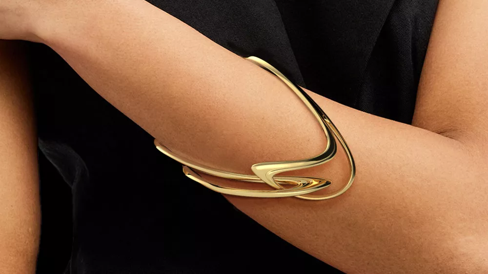 یک دستبند طلا با طرح خاص و هنری در دست زنی با لباس مشکی