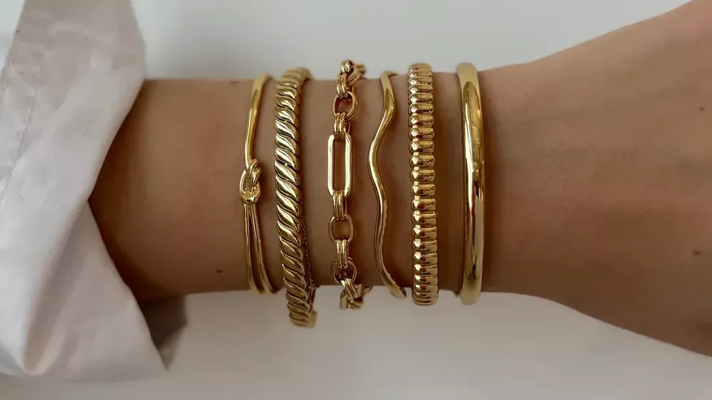 چندین دستبند طلا در دست زنی با پیراهن سفید