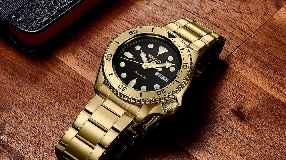 ساعت Seiko Smart Gold Watch با قاب و دستبند طلایی و صفحه مشکی روی میز چوبی