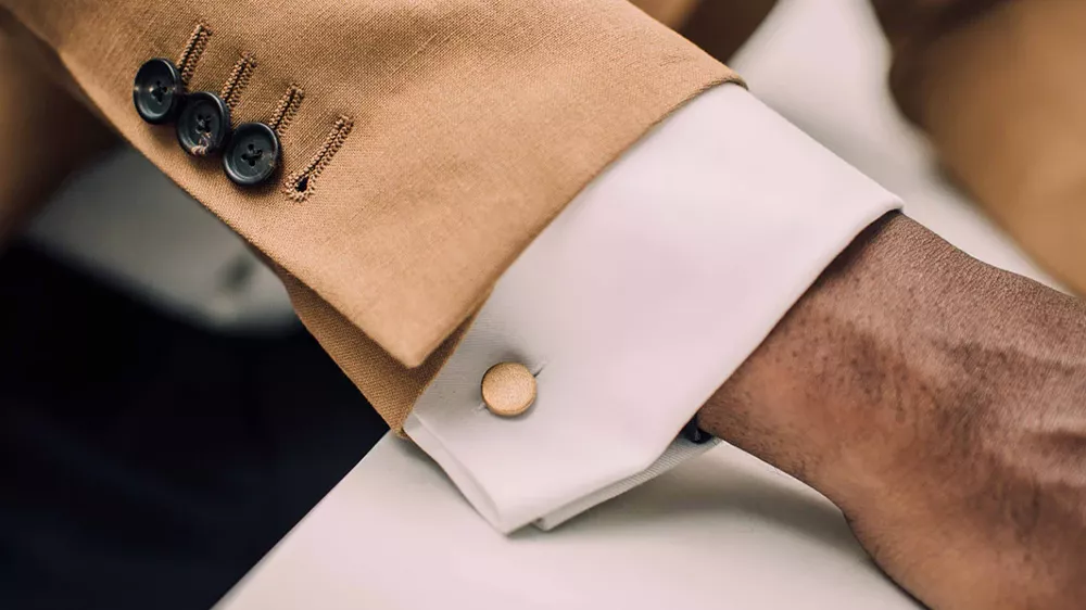 دکمه سردست مینیمال روی پیراهن سفید مردی با کت و شلوار قهوهای