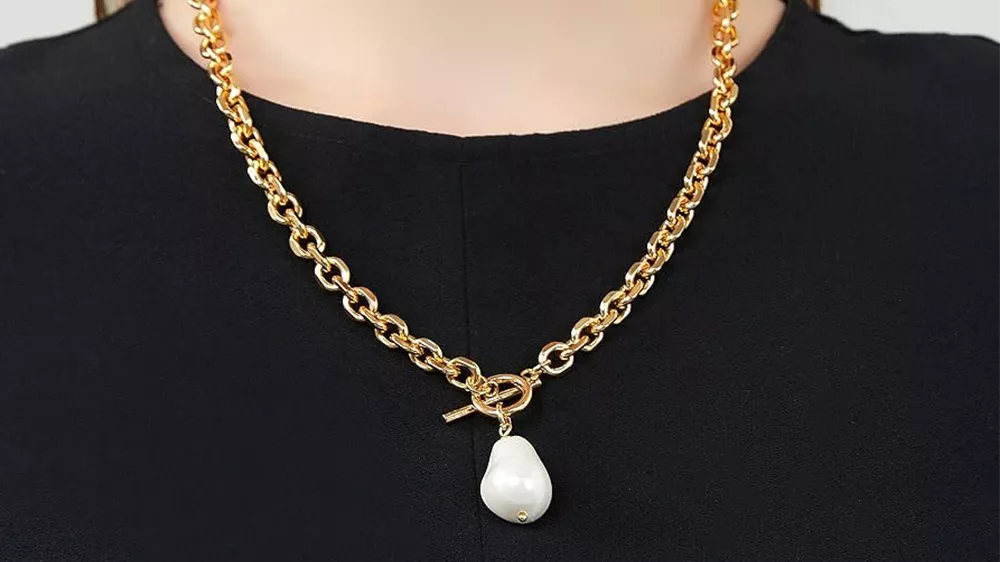 یک گردنبند با مروارید Baroque با زنجیر طلا در گردن زنی با لباس مشکی