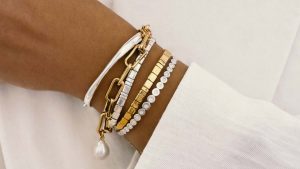 چند دستبند با طلای زرد و طلای سفید در دست یک زن با لباس سفید