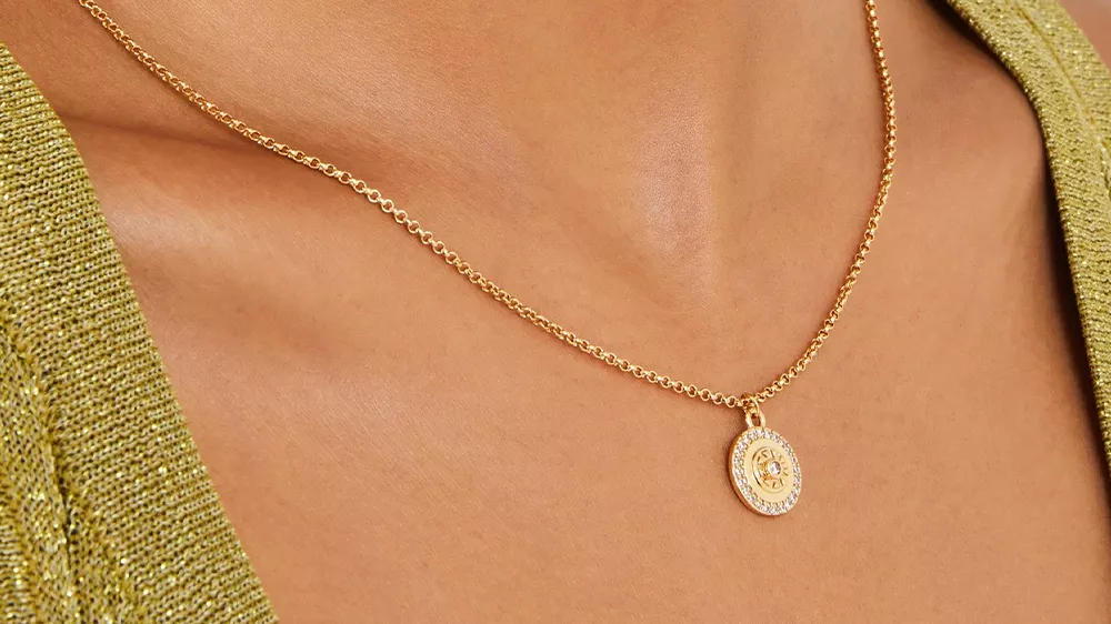 یک زنجیر طلا با یک پلاک در گردن زنی با لباس سبز